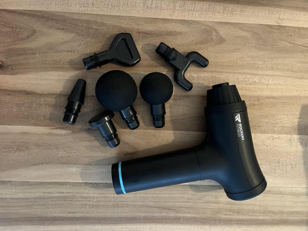 afbeelding van de rockerz fitness massage gun met alle 6 de opzetstukken op tafel